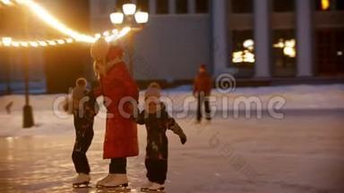 一家人的母亲和两个孩子晚上在明亮的灯光下在公共冰场上滑冰